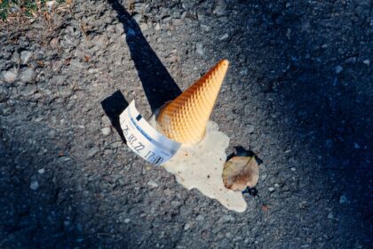 A dropped ice cream cone melting on the asphalt with a parking ticket nearby.