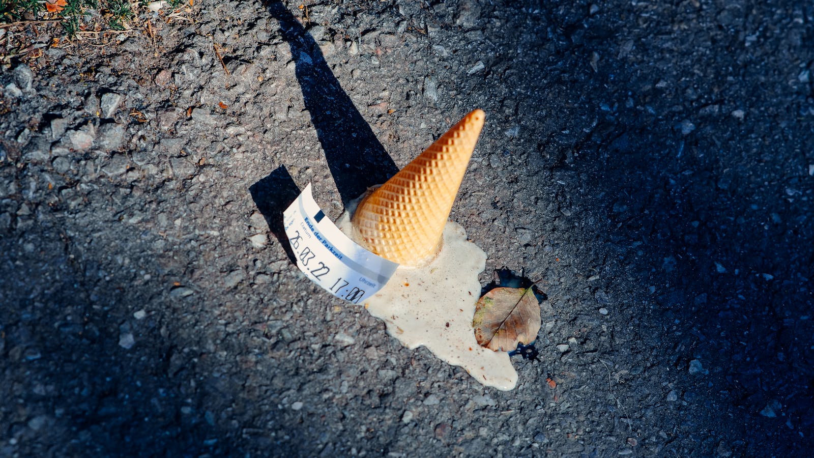 A dropped ice cream cone melting on the asphalt with a parking ticket nearby.