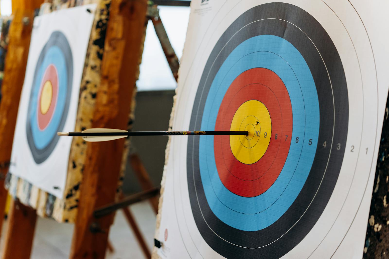An arrow hits the bullseye on a colorful target in an indoor archery range.