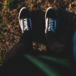A top-down view of a person standing on a dirt path wearing casual sneakers, captured in warm natural light.