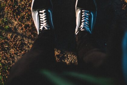 A top-down view of a person standing on a dirt path wearing casual sneakers, captured in warm natural light.