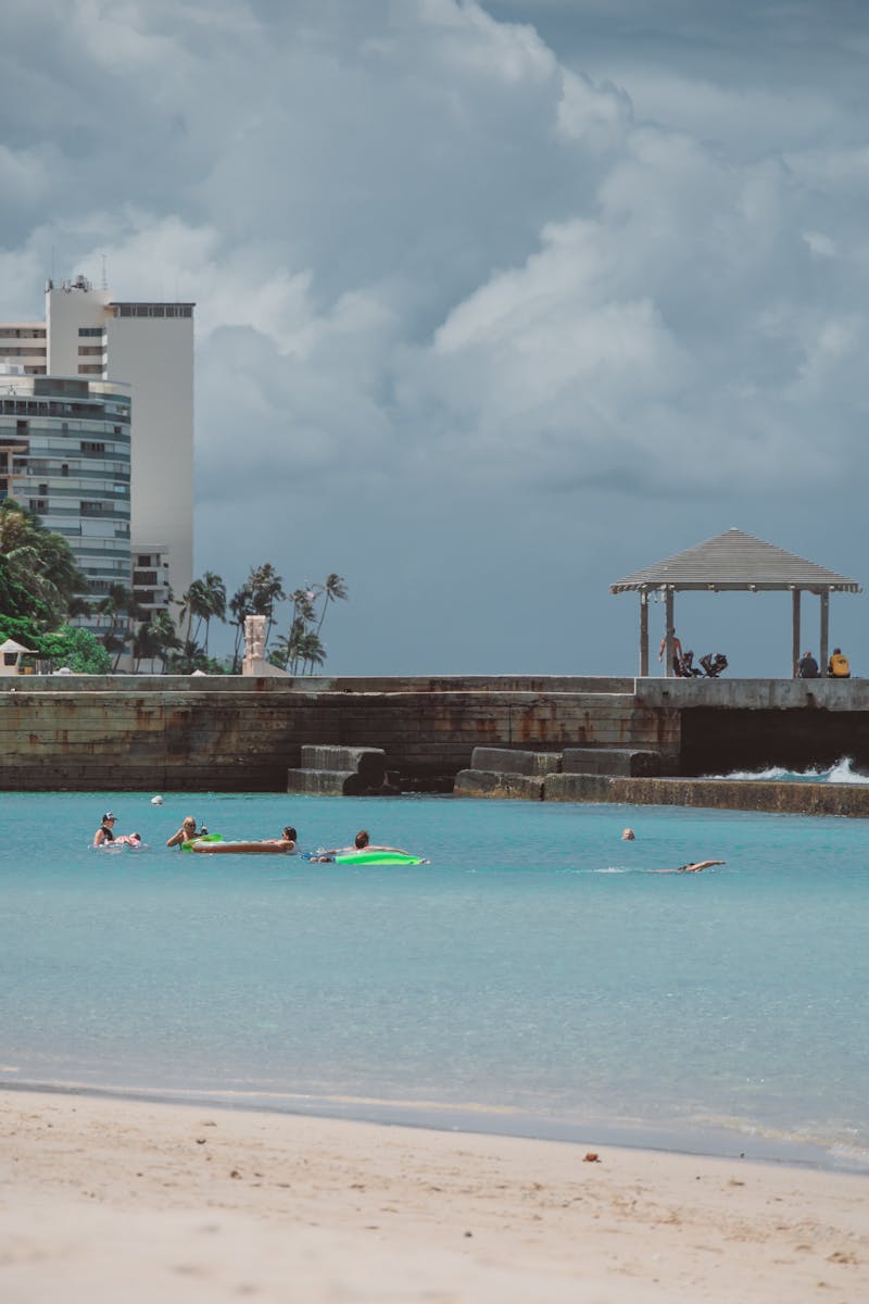 People enjoying a tropical beach with turquoise sea and modern buildings in the background.